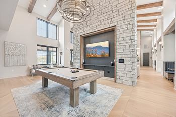 A pool table is in the middle of a room with a stone wall and a painting hanging above it.